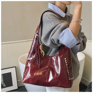 Close-up of burgundy glossy leather shoulder bag with silver studs and tassel detail