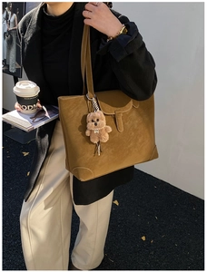Detail of tan suede tote bag with white stitching and a cute teddy bear charm