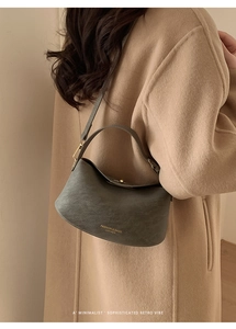 Detail shot of grey faux leather shoulder bag with gold text on earth-tone trench coat