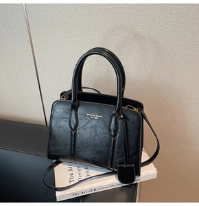 Detail of black glossy oil wax textured tote bag with brand logo and dual handles