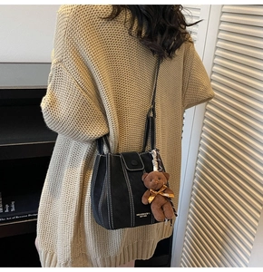 Detail of black bucket bag with white contrast stitching and plush bear charm