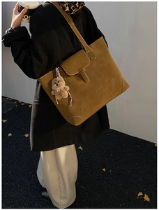 Macro detail of brown suede tote bag with white stitching and plush bear charm