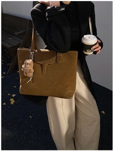 Detailed view of a vintage tan suede tote bag with a decorative buckle and plush bear charm