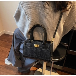 Detail of black crocodile texture handbag with gold metal clasp on a model