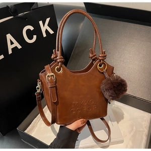 Detail of dark brown leather bucket bag showing MKXQ COEOR embossed logo and plush ball charm