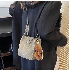 Detail of retro bucket bag in sage green with brown teddy bear charm on black blazer