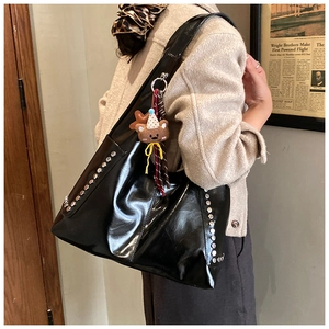 Détail du sac cabas noir brillant avec des rivets argentés et un pendentif ours en peluche