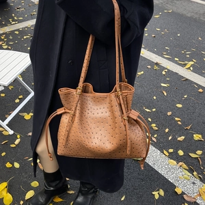 Brown ostrich textured tote bag with drawstring and gold hardware shown on a city street