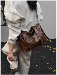 Deep brown oversized glossy PU leather tote bag with side ties shown in autumn street scene