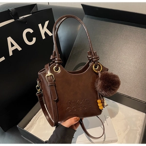 Detail of dark brown glossy bucket bag with metal ring handle and plush ball charm