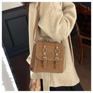 Detail of vintage brown leather messenger bag with gold buckles on a wool coat