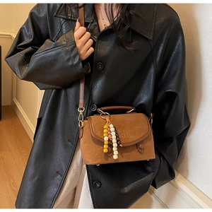 Close-up of brown vintage crossbody bag with wood bead charm and embossed logo