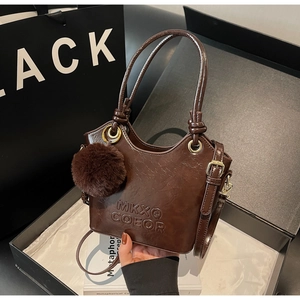 Detail of vintage brown bucket bag with plush charm and embossed logo on glossy leather