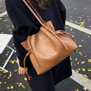 Detail of ostrich embossed texture on brown drawstring tote bag worn over black coat