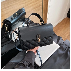 Detail view of black leather handbag featuring quilted pattern and gold metal hardware lock