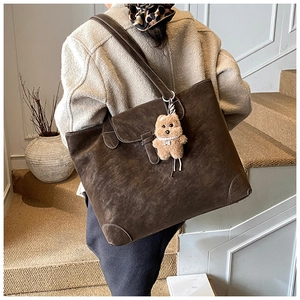 Detail of vintage dark brown tote bag with a plush bear charm on a model's shoulder