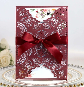 Detail of burgundy laser-cut wedding invitation with silk bow on decorative plate