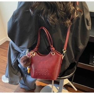 Detail of wine red bucket bag with embossed lettering and plush ball charm on shoulder