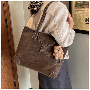Detail of a brown vintage tote bag with flap lock and cute plush bear charm accessory