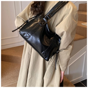 Detail of black glossy leather tote with silver buckle and decorative side straps