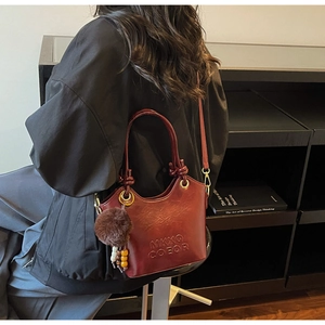 Detailed close-up of retro burgundy leather bucket bag with embossed logo and fuzzy pompom