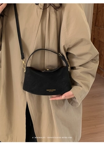Detail of black leather bucket bag with gold logo on a model wearing a beige trench coat