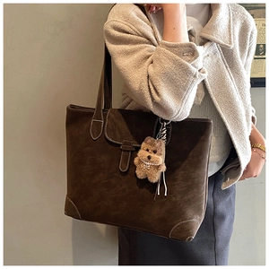 Detail of dark brown matte leather tote bag with a cute plush puppy pendant