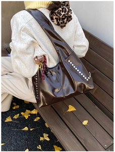 Détail d'un sac vintage en cuir brillant marron foncé avec rivets argentés et ours décoratif