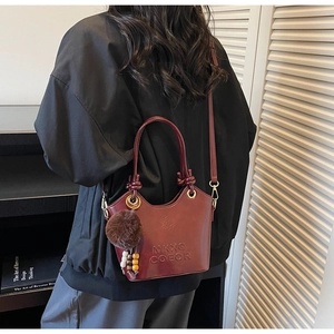 Detail view of deep red bucket bag with textured leather and plush pompom charm decoration