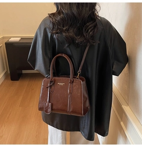 Detail of dark brown glossy leather tote bag with golden logo and slender shoulder strap