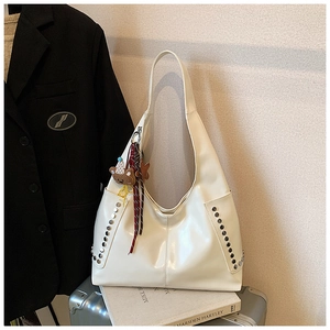 Détail du sac hobo blanc clouté avec pendentif ours et ruban rouge sur une valise rétro