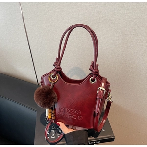 Detail of vintage burgundy bucket bag with embossed logo and fuzzy pom-pom accessory