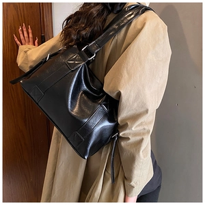 Close-up of vintage black glossy PU leather shoulder bag with wide strap and cross-stitching
