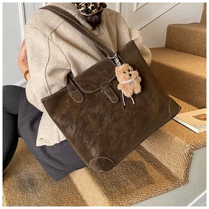 Close-up of vintage brown tote bag with contrast stitching and teddy bear charm