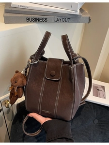 Retro dark brown bucket bag with contrast stitching, top handles and plush bear charm