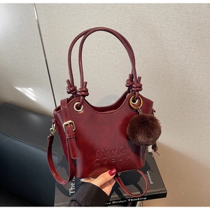 Detail of burgundy glossy bucket bag with knot handle and brown faux fur pompom charm
