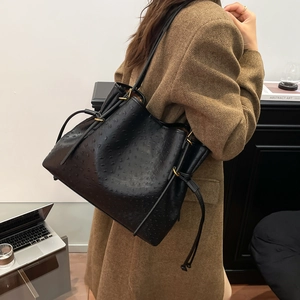Detail of black ostrich-embossed tote bag with golden hardware on a model shoulder