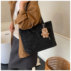 Detail of black suede tote bag featuring a magnetic flap and a cute teddy bear charm