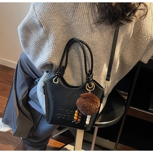 Detail of black bucket bag with embossed letters, brown pompom and beaded charm