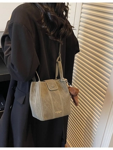 Deep greyish-green bucket bag with contrast stitching and brown bear charm on black coat