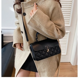 Detail of black quilted leather handbag with gold oval twist lock worn on a beige wool coat