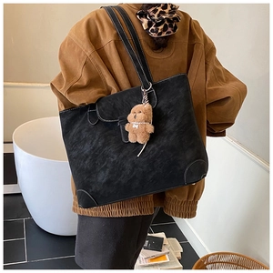 Detail of black tote bag with white contrast stitching and a plush bear pendant charm