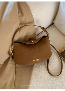 Close-up of brown suede handbag with gold hardware and embossed fashion logo lettering