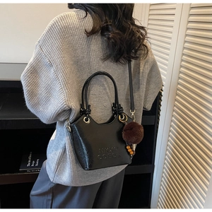 Detail of black faux leather bucket bag with top handle and brown fur pom pom charm