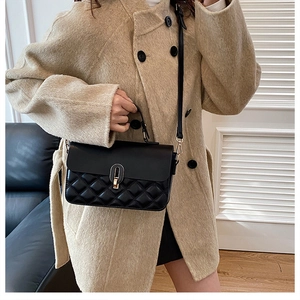 Close-up of black quilted leather handbag with metal turn-lock on a beige wool coat