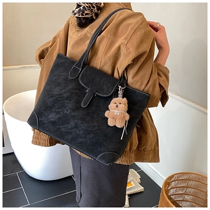 Macro detail of black tote bag featuring white contrast stitching and plush bear charm