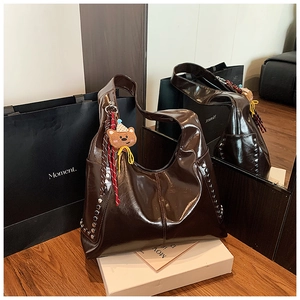 Détail du sac hobo en cuir brillant marron foncé avec rivets et breloque ours incluse