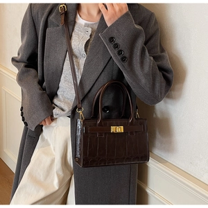 Detail of a brown crocodile texture handbag with gold hardware and shoulder strap