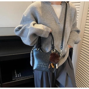Detail of black textured bucket bag with fur ball charm and brand lettering