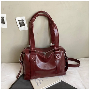 Detail view of smooth burgundy leather tote bag with sturdy stitched handles on white fabric
